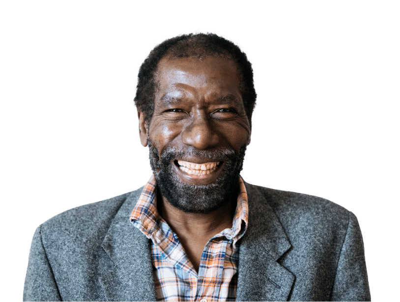 A middle-aged man with a beard, wearing a gray blazer over a plaid shirt, smiles warmly at the camera against a plain background.