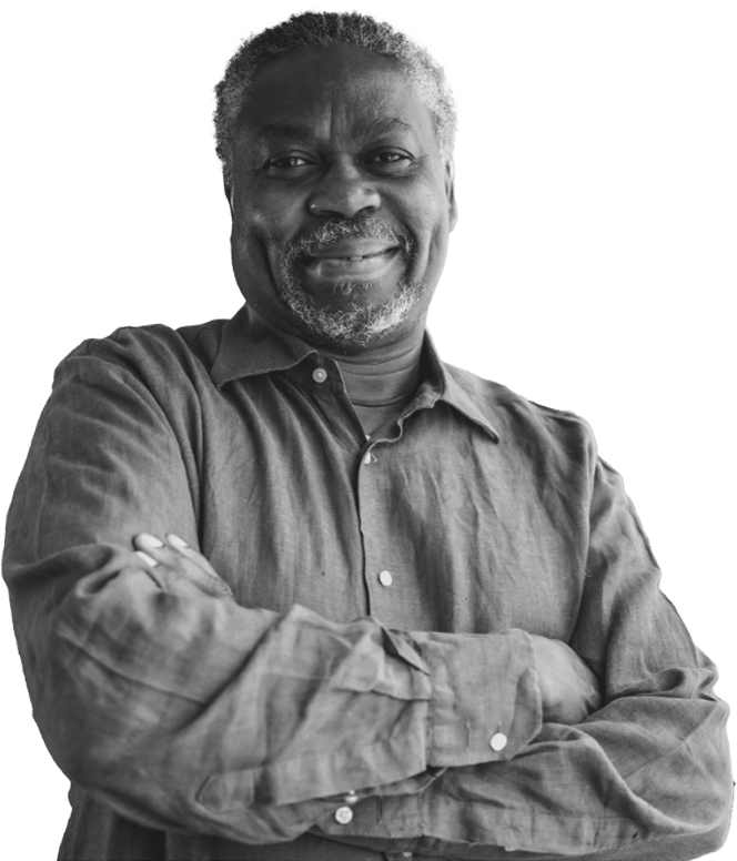 A man with gray hair and a beard smiles with his arms crossed, wearing a button-up shirt. The photo is black and white, and the background is plain white.