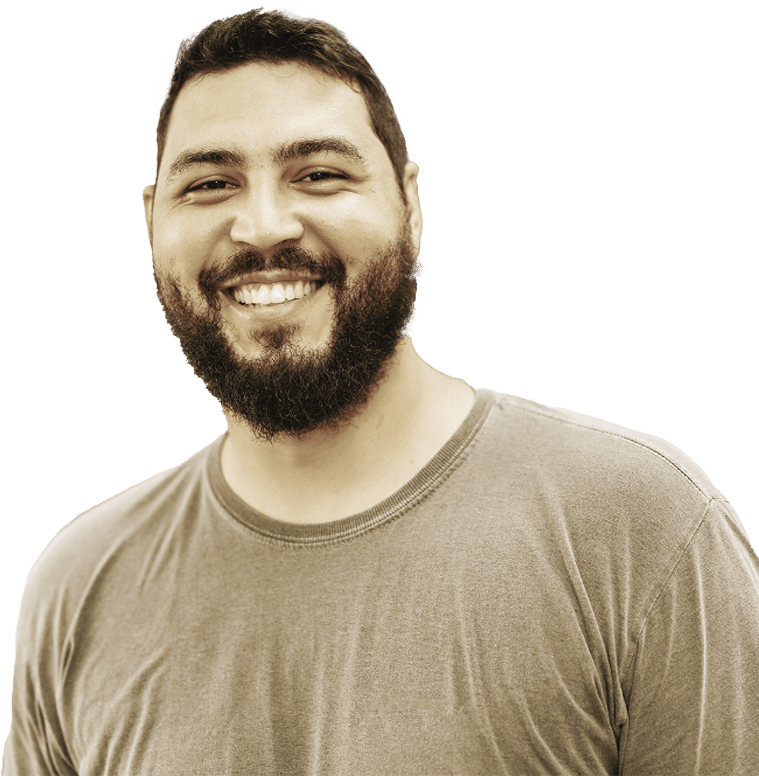 A man with a beard and short hair smiles warmly at the camera, wearing a plain, light-colored t-shirt against a white background.