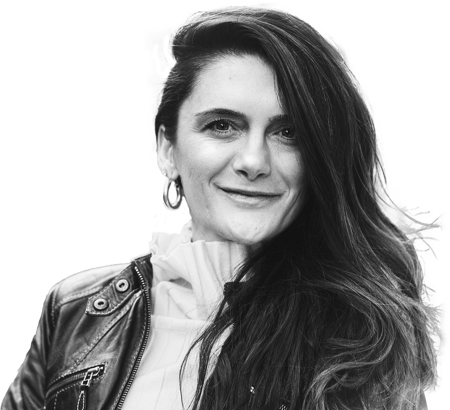 A woman with long, wavy hair smiles gently at the camera. She is wearing a leather jacket over a ruffled top. The image is black and white with a blurred background.