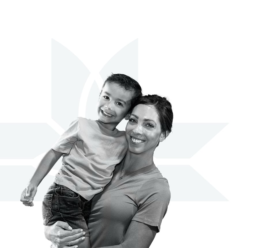 A smiling woman holds a young boy in her arms. Both are wearing casual t-shirts. The background is white with a faint geometric floral design.