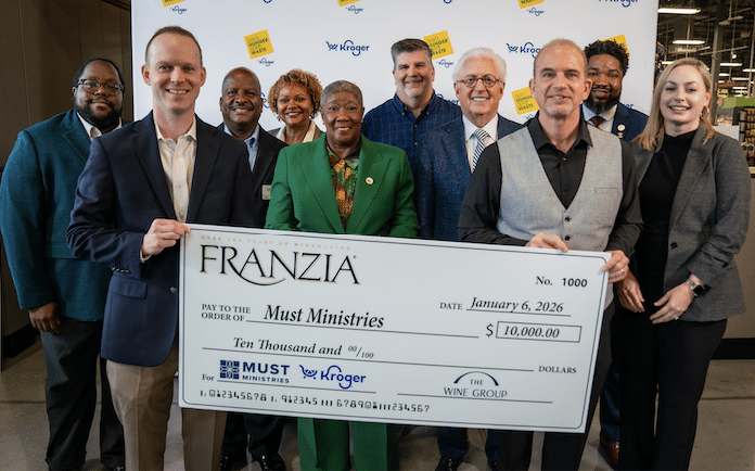 A group of people pose indoors, smiling and holding an oversized $10,000 food donation check for Must Ministries from Franzia, dated January 6, 2026, with Kroger, Must Ministries, and The Wine Group logos in support of a neighborhood pantry.
