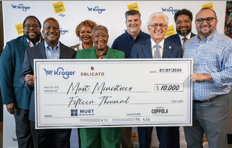Eight people stand smiling and holding a large ceremonial Kroger and Delicato check for $15,000 made out to Must Ministries, supporting the fight against food insecurity, against a white background with Kroger logos.